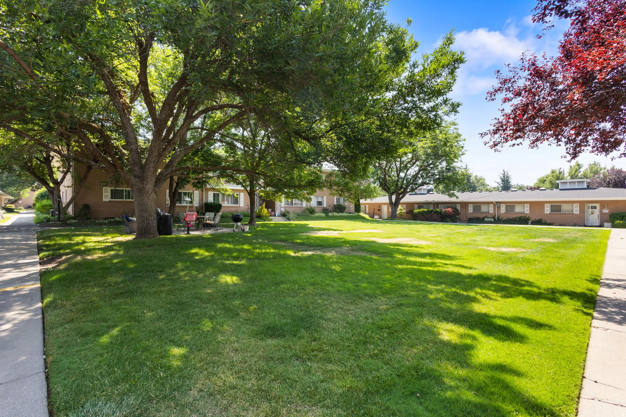 Expansive green space featuring a manicured lawn, mature shade trees, and brick-faced buildings with multiple white-shuttered windows