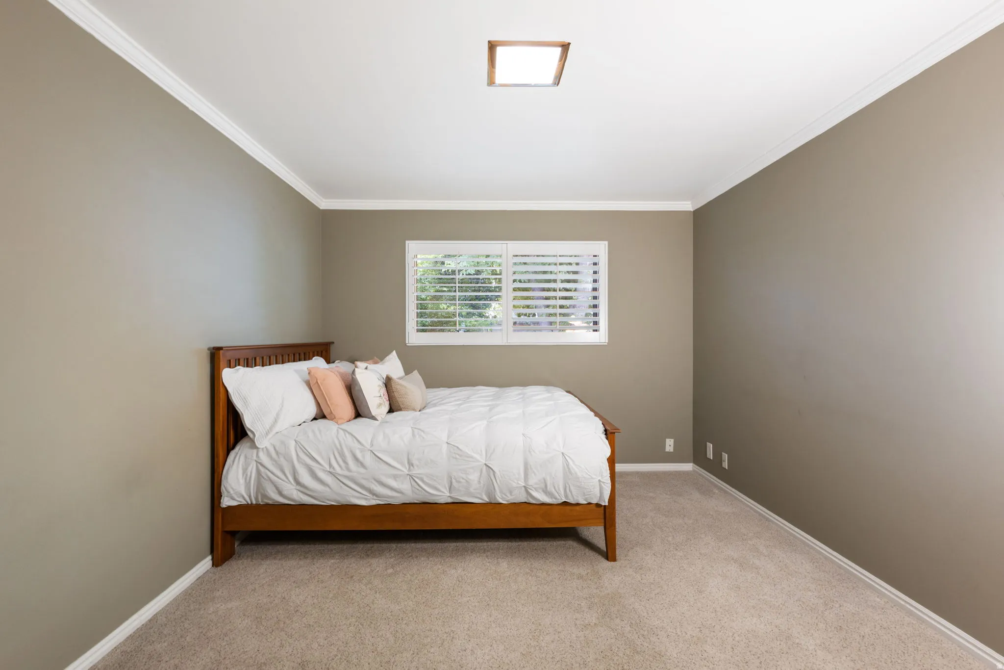 Carpeted room with a window featuring white plantation shutters, crown molding, and a flush-mount ceiling light fixture