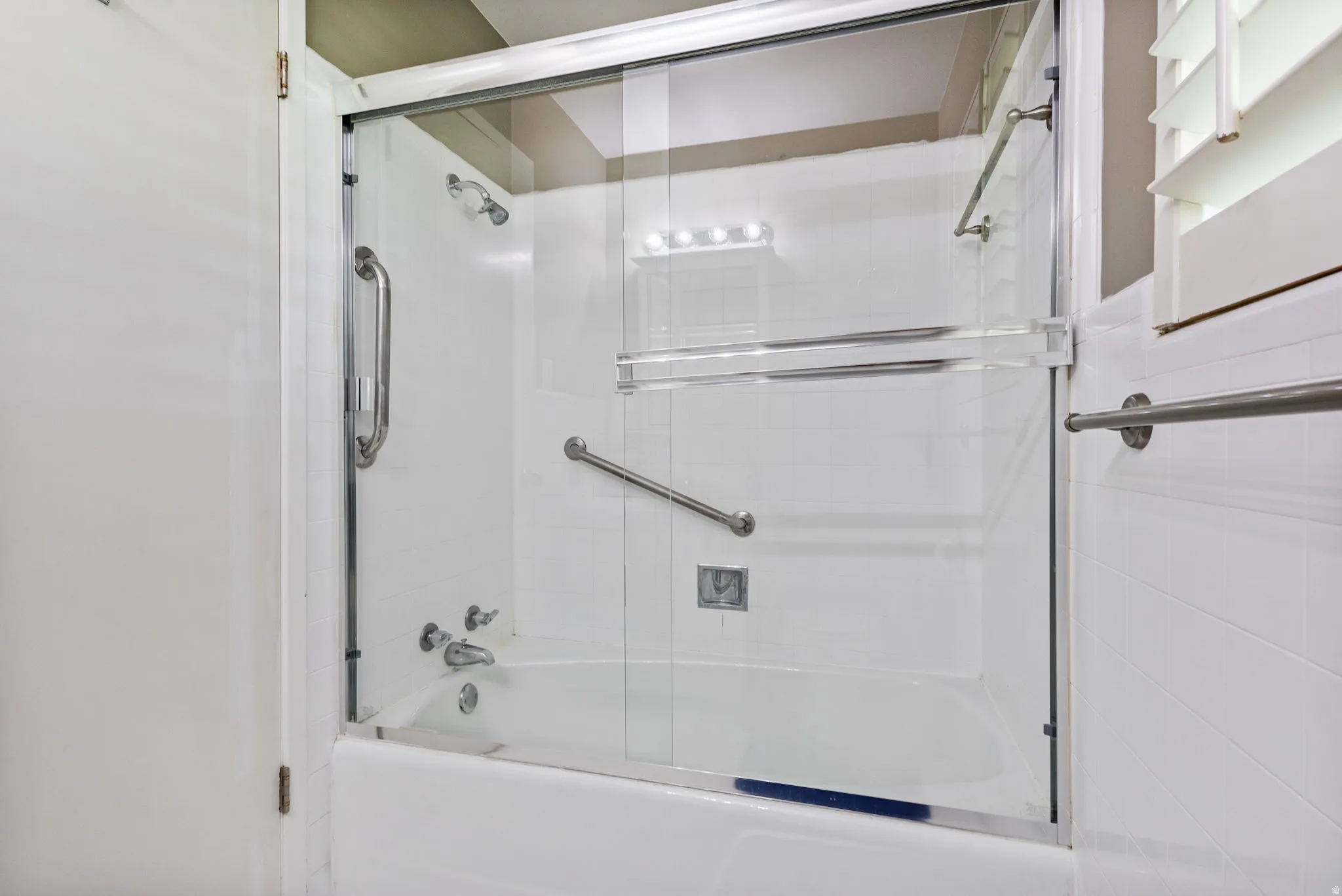 Bathtub and shower combination featuring a glass enclosure, white tile surround, and brushed nickel fixtures