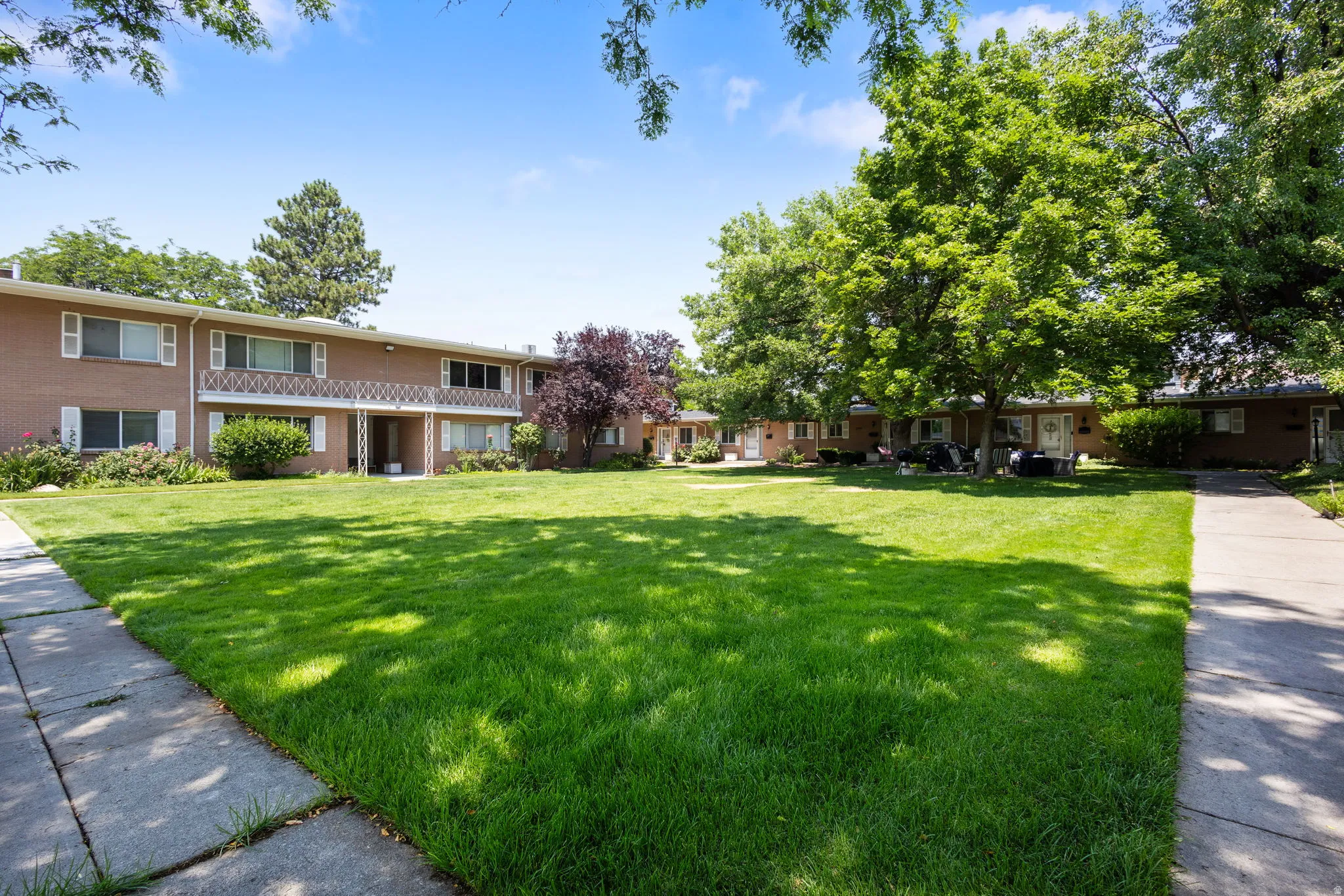Expansive common green space with mature trees, flanked by brick exterior buildings featuring white shutters and balconies with decorative railings