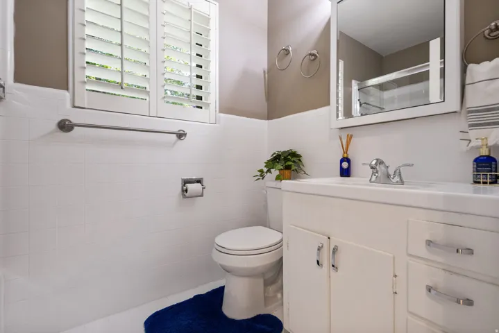 Bathroom featuring white tiled walls, a white vanity with integrated sink, white cabinetry with chrome hardware, and a white framed mirror