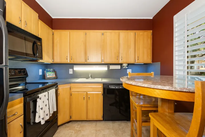 Kitchen featuring light wood cabinetry, black appliances, solid surface countertops, and a built-in breakfast bar
