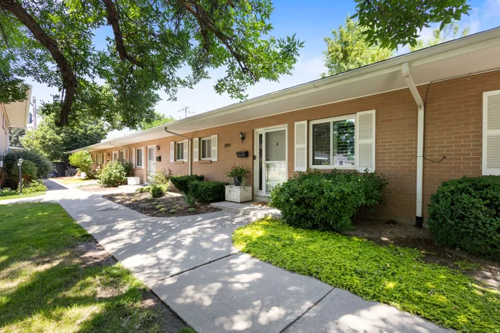 Brick exterior featuring white window shutters, a covered walkway, and mature landscaping
