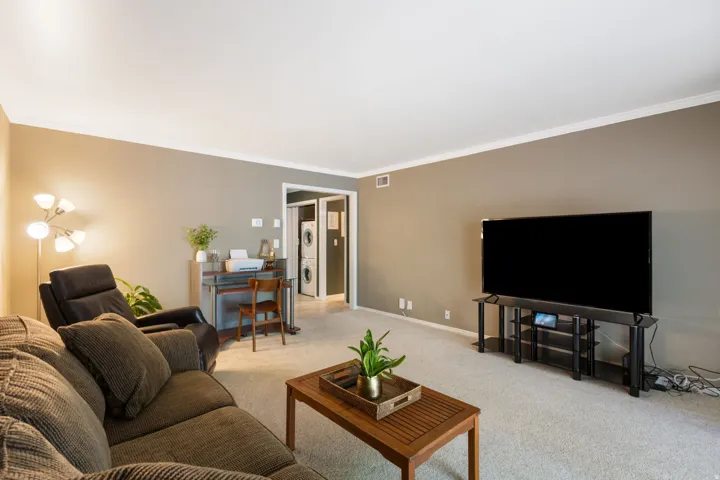 Living area featuring neutral wall tones, crown molding, and carpeted flooring