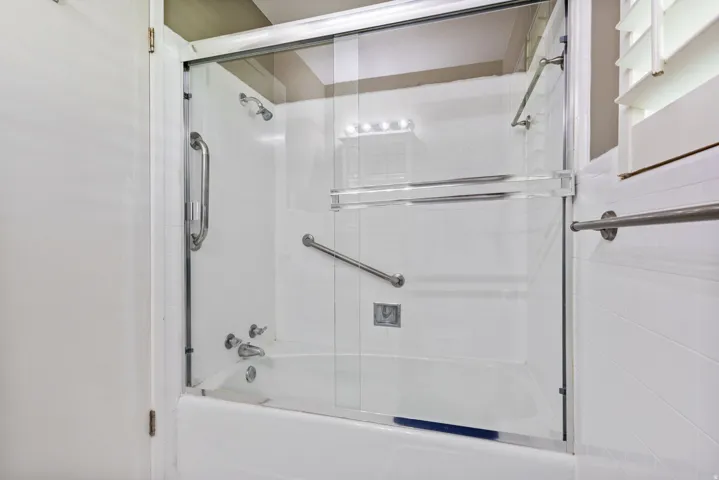 Bathtub and shower combination featuring a glass enclosure, white tile surround, and brushed nickel fixtures