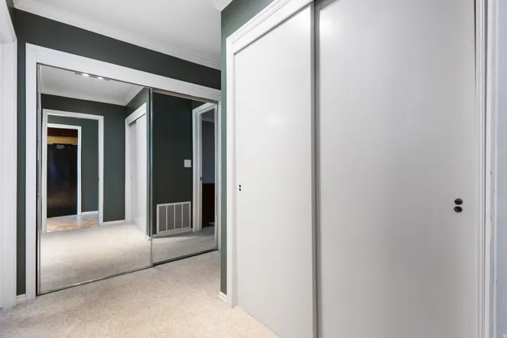 Hallway featuring mirrored sliding closet doors with white trim, dark painted walls, and light carpeting