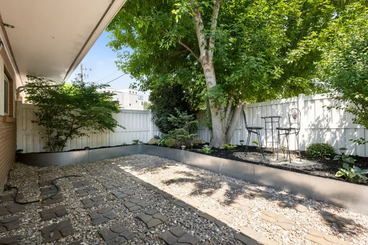 Landscaped outdoor space featuring a gravel and paver patio, a white privacy fence, mature trees, and raised garden beds with established plantings