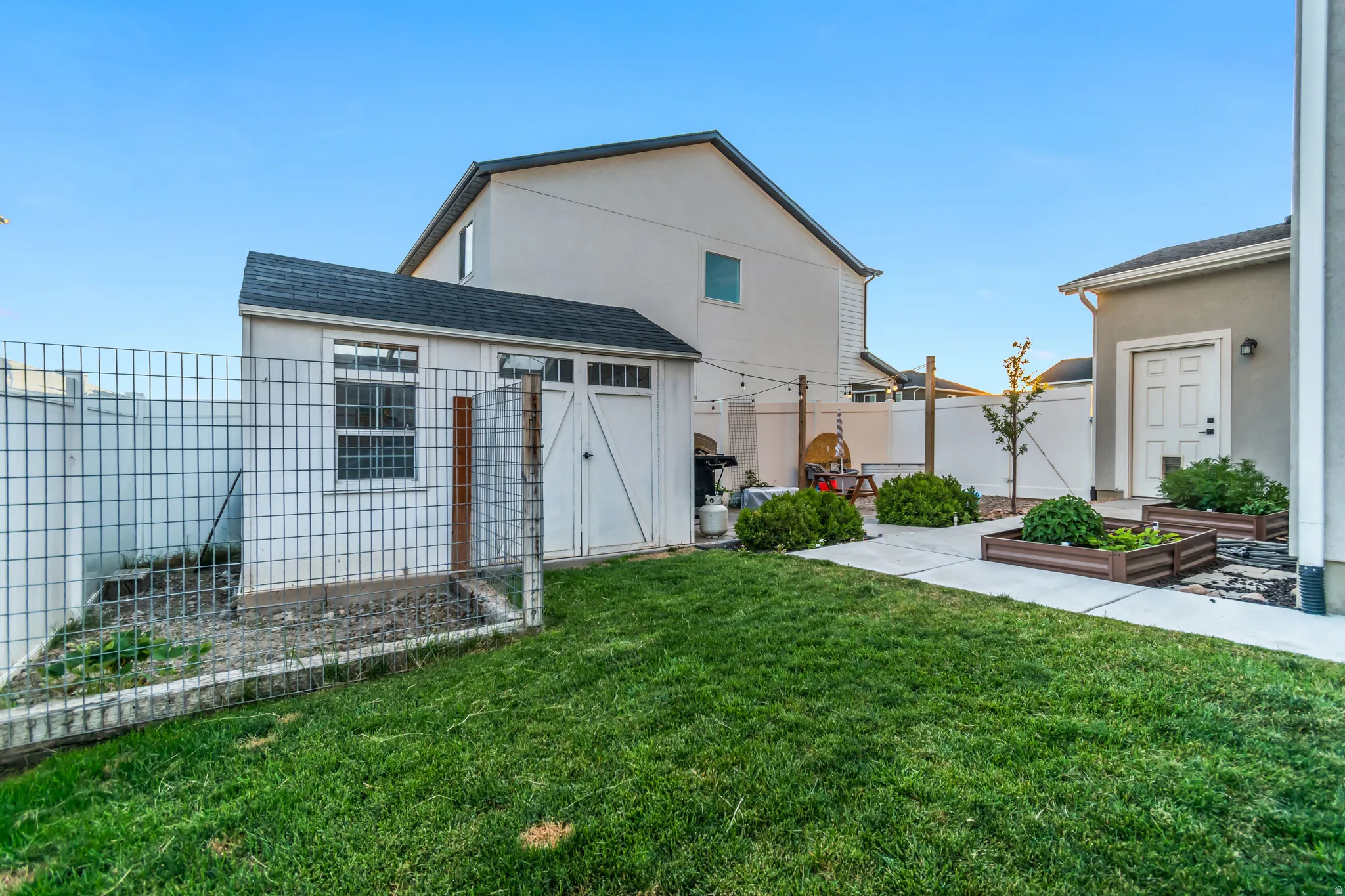 Expansive backyard featuring a manicured lawn, concrete patio area, and raised garden beds