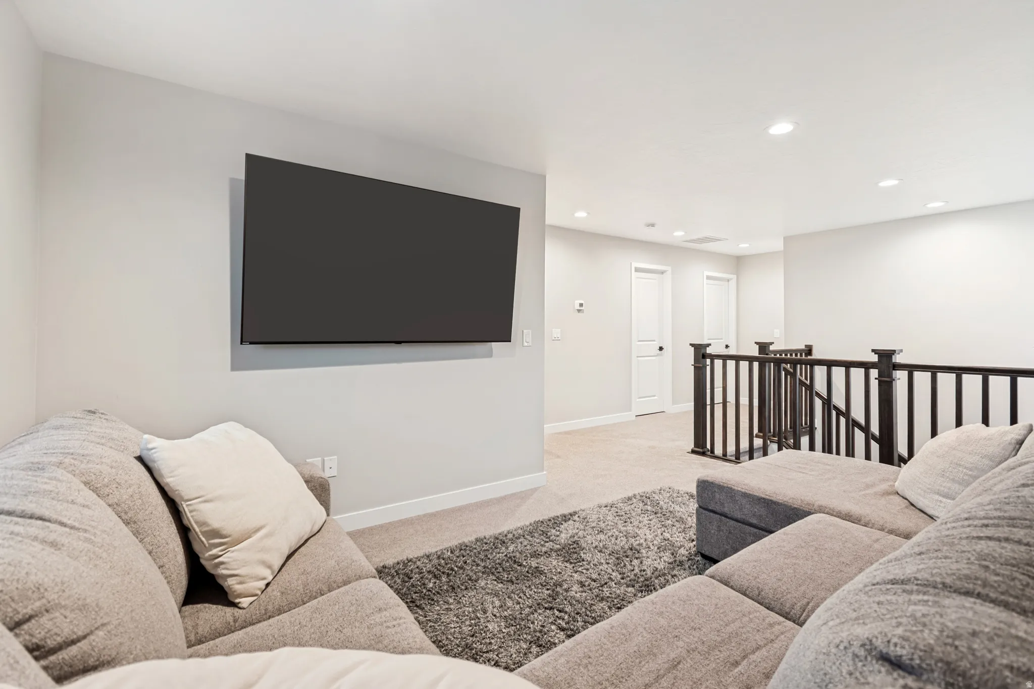 Spacious upper-level landing featuring neutral carpeting, a wall-mounted television, recessed lighting, and dark wood-finish balusters