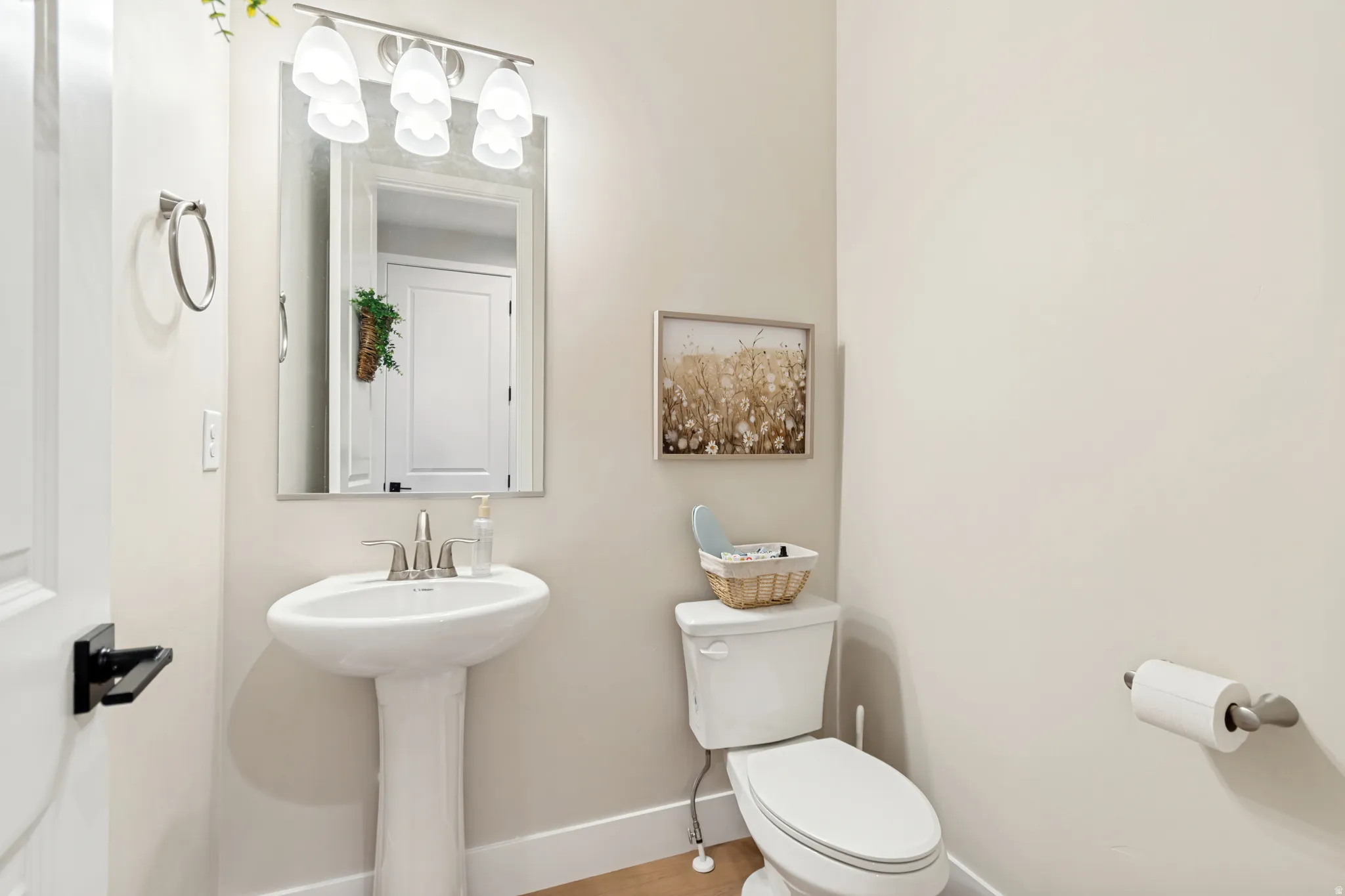 Pedestal sink with chrome faucet, complemented by a rectangular mirror and three-light vanity fixture