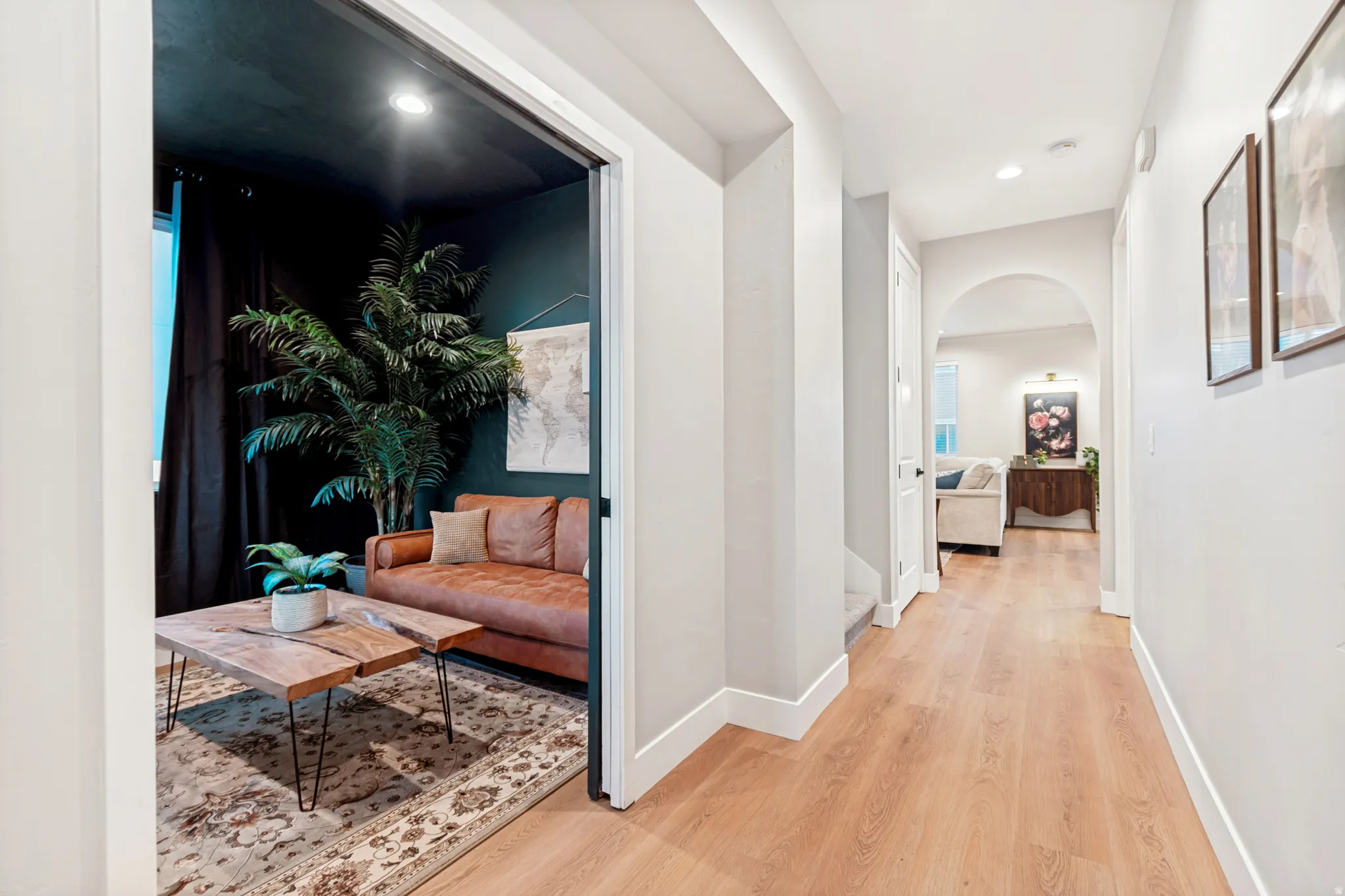 Hallway with wood-finish flooring, white baseboards, light gray walls, and an arched doorway