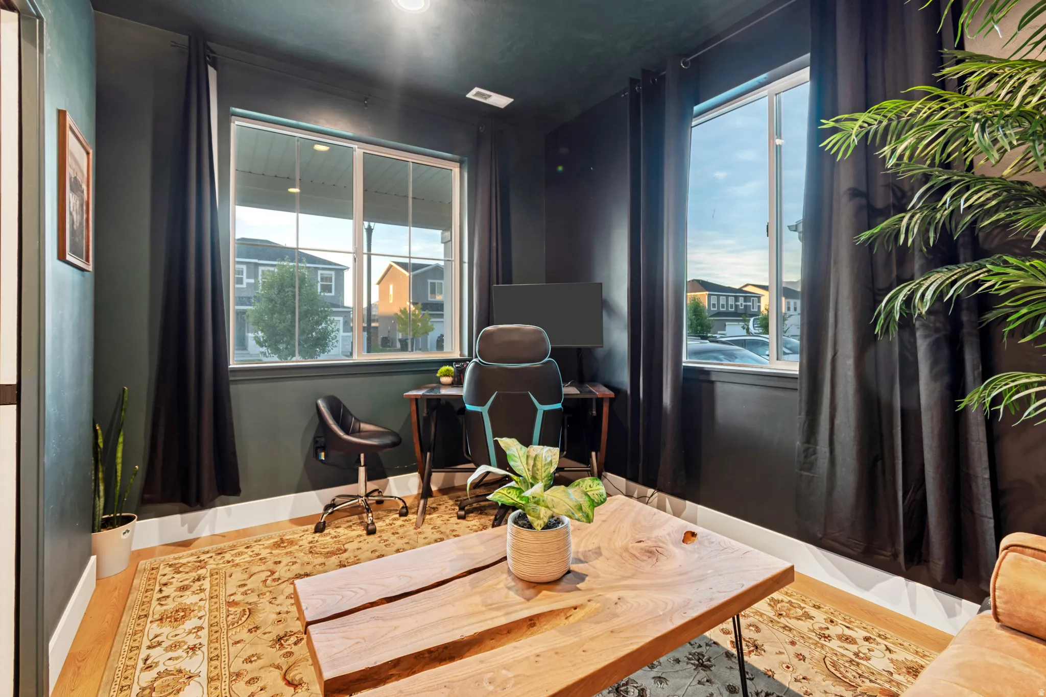 Room featuring dark accent walls with white trim, wood-finish flooring, and two large windows