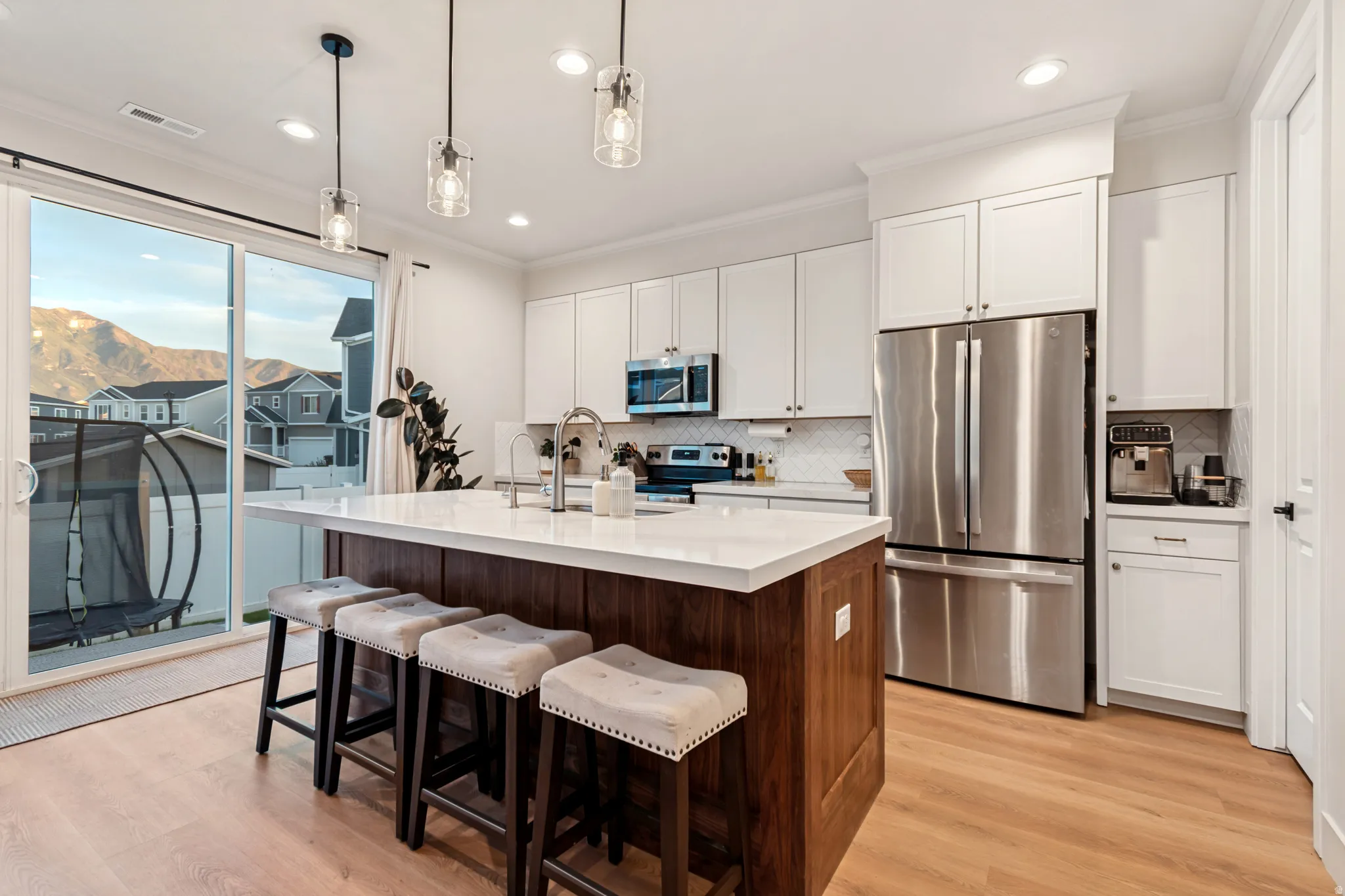 Modern kitchen featuring white shaker cabinetry, stainless steel appliances, a center island with a wood-finish base and light-toned countertop, and light wood-finish flooring