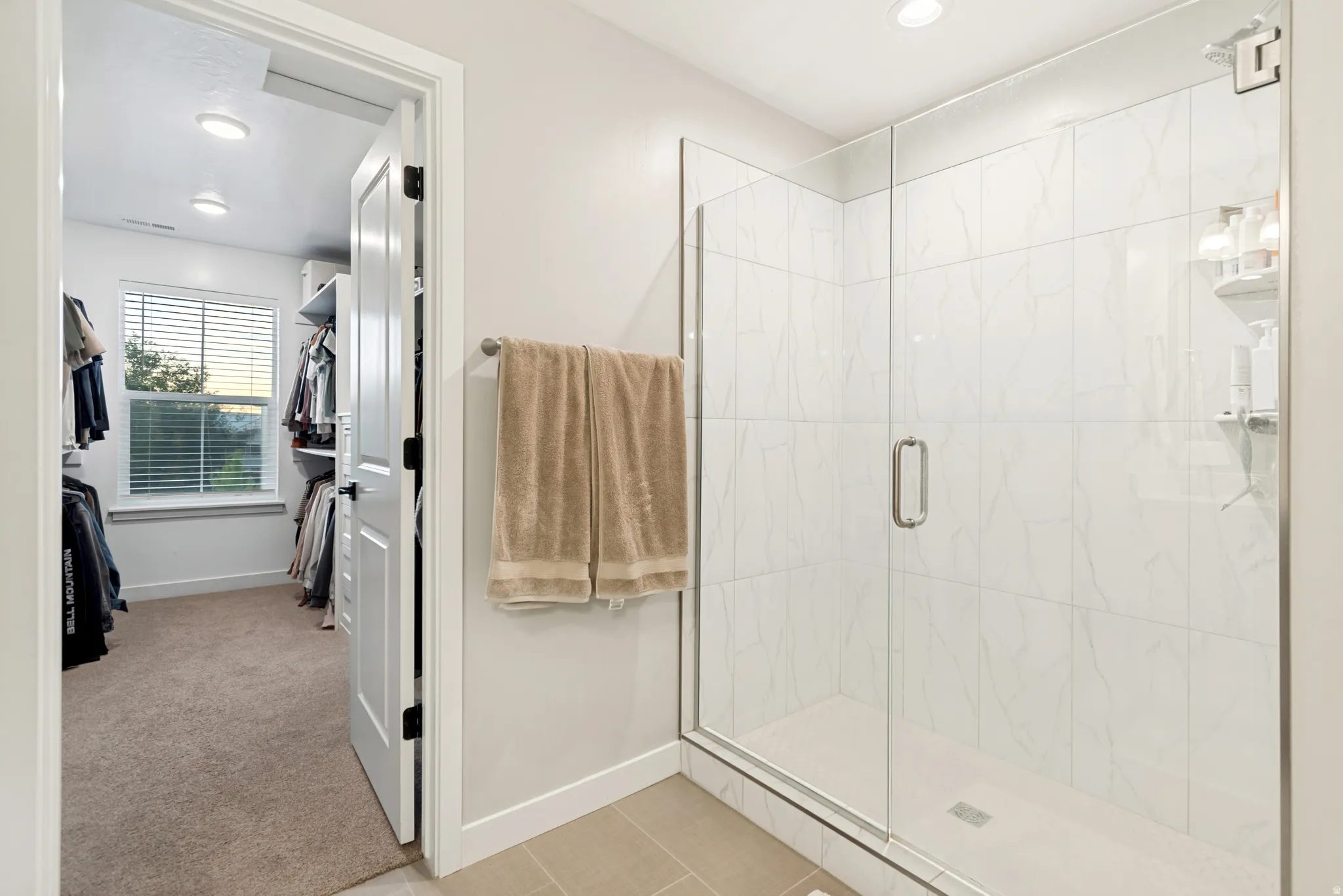 Glass-enclosed shower featuring white tile surround and a built-in shelf, with tile flooring