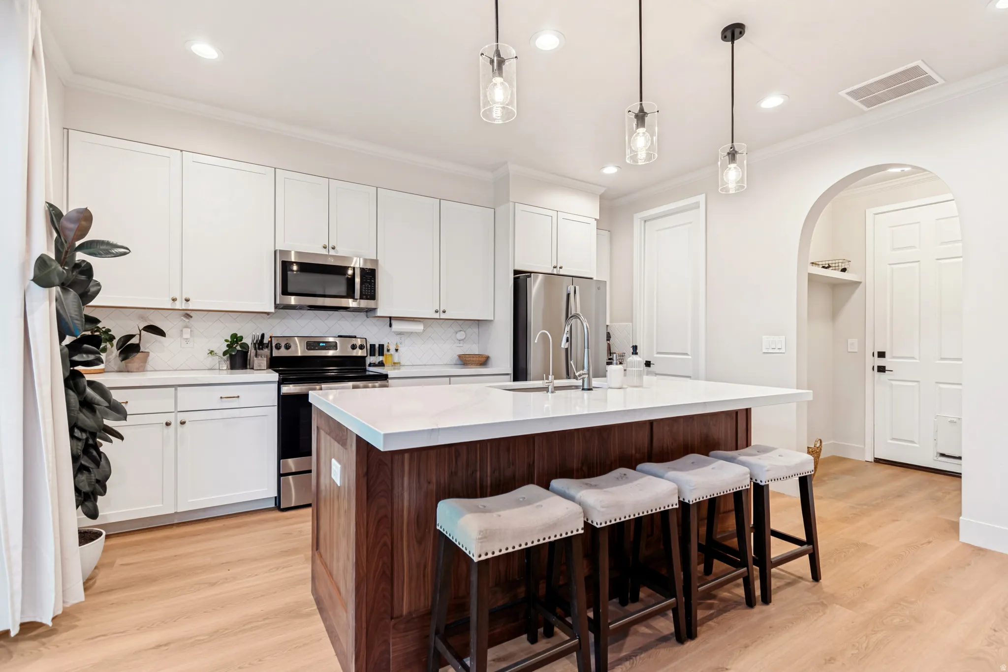 Kitchen featuring a wood-finish island with seating, white shaker cabinetry, stainless steel appliances, and wood-finish flooring