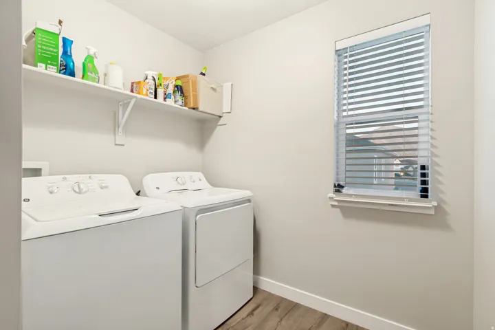 Dedicated laundry area featuring a white shelving unit, wood-finish flooring, and a window with horizontal blinds