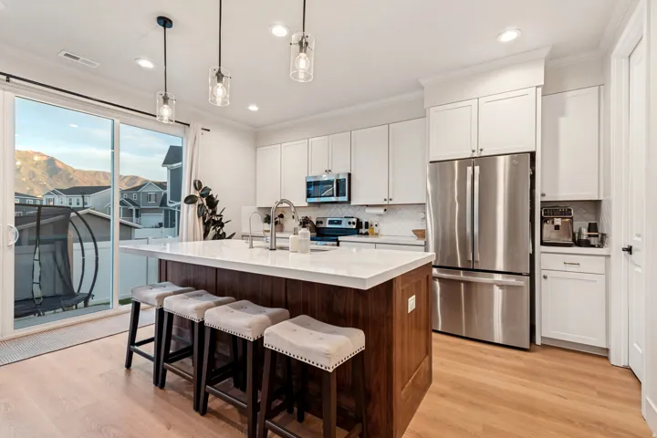 Modern kitchen featuring white shaker cabinetry, stainless steel appliances, a center island with a wood-finish base and light-toned countertop, and light wood-finish flooring
