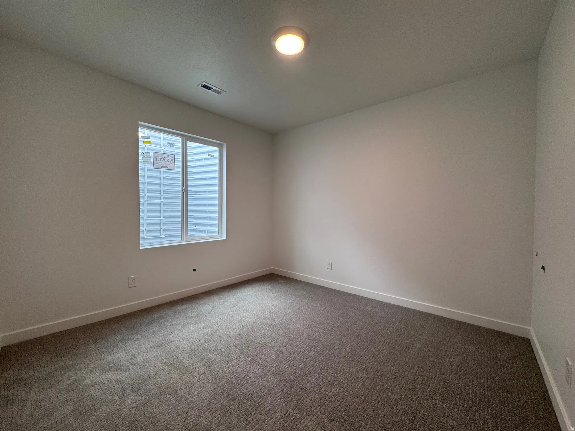 Interior room featuring light neutral wall paint, a single window, a ceiling-mounted light fixture, and textured carpet flooring