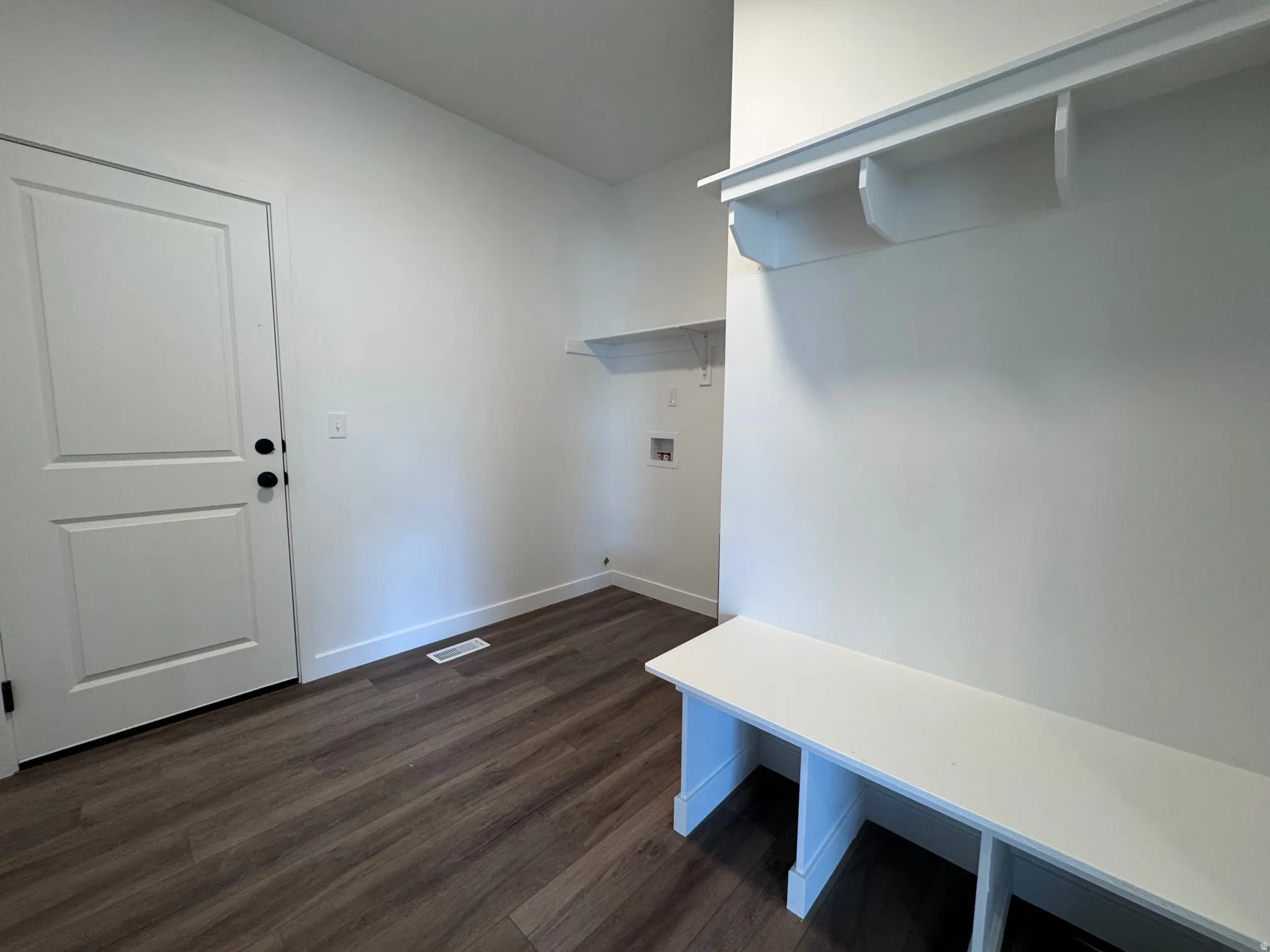 Mudroom featuring wood-finish flooring, built-in storage bench, wall-mounted shelving, and laundry appliance hookups