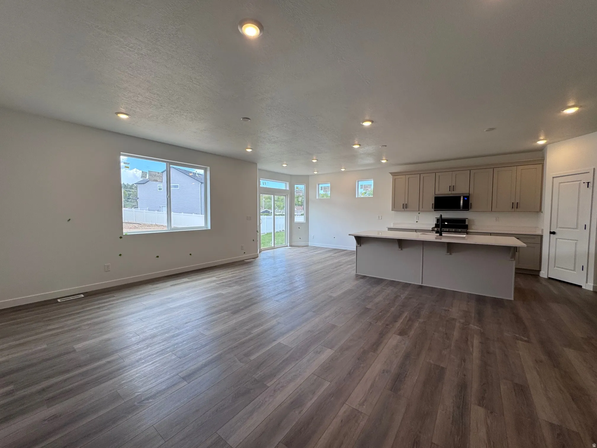 Open-concept living area featuring wood-finish flooring, recessed lighting, a modern kitchen island with countertop seating, light-toned cabinetry, and sliding glass door access to the exterior