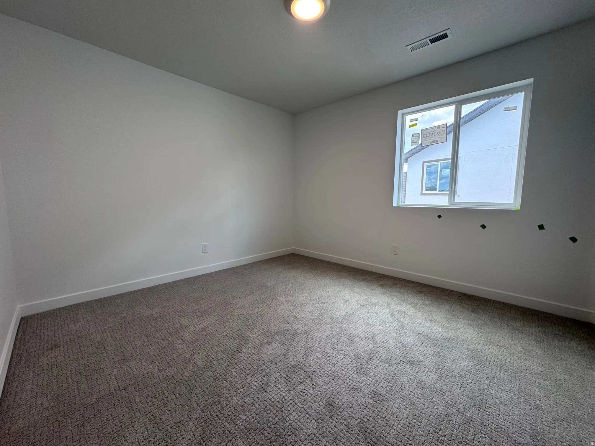 Spacious room featuring neutral carpeting, white walls, a white trim baseboard, and a large window