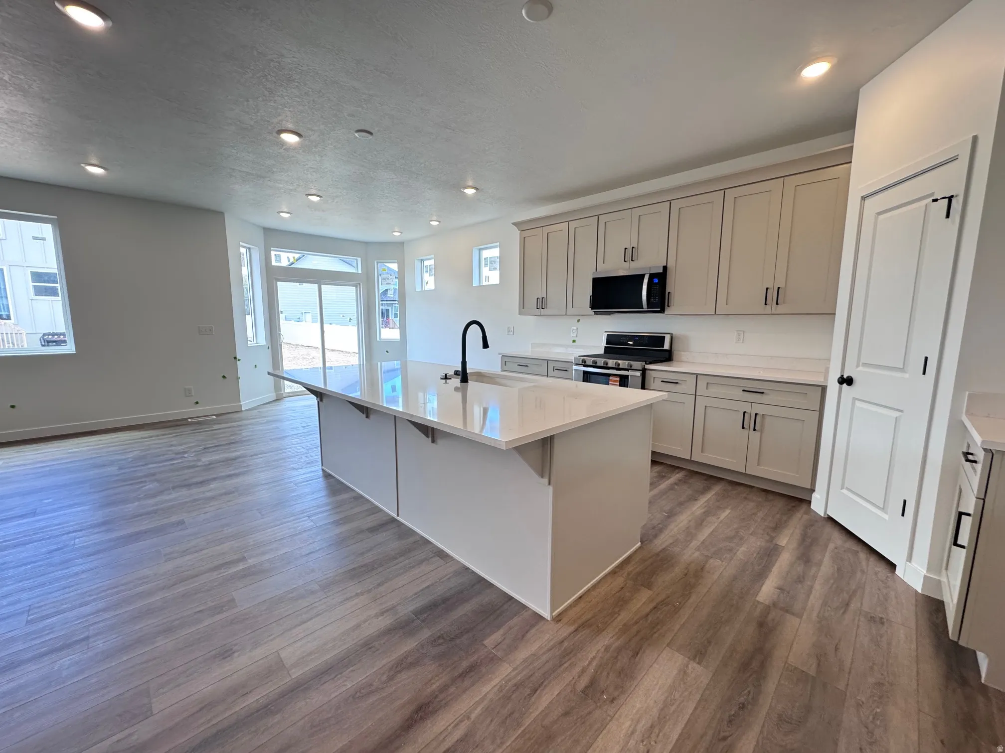 Kitchen featuring an expansive center island with a quartz countertop, wood-finish flooring, recessed lighting, stainless steel appliances, and cream-colored cabinetry