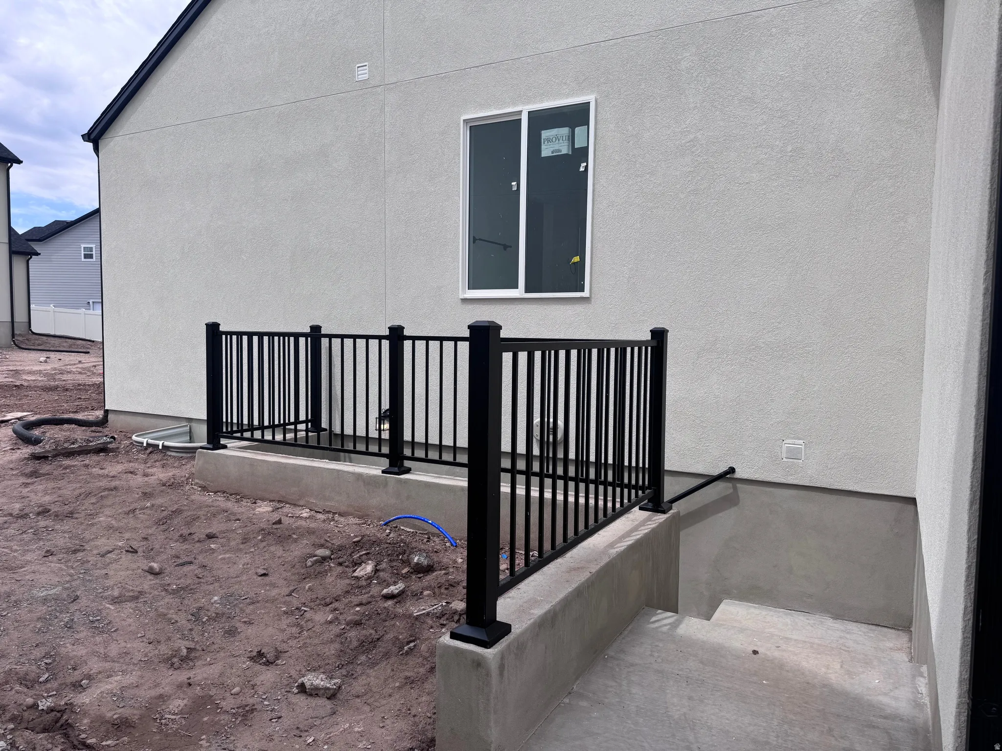 Exterior stucco finish with black aluminum railing leading to a concrete basement entry