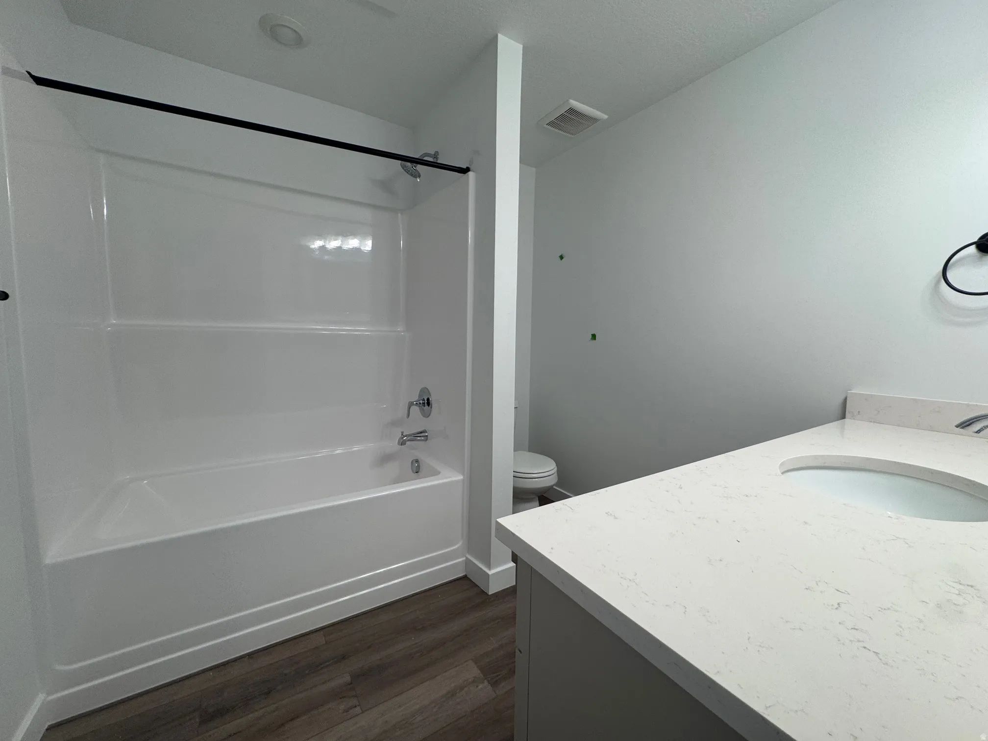 Bathroom featuring a white tub-shower combination with a chrome faucet, a vanity with a light-colored countertop and an integrated sink, and wood-finish flooring