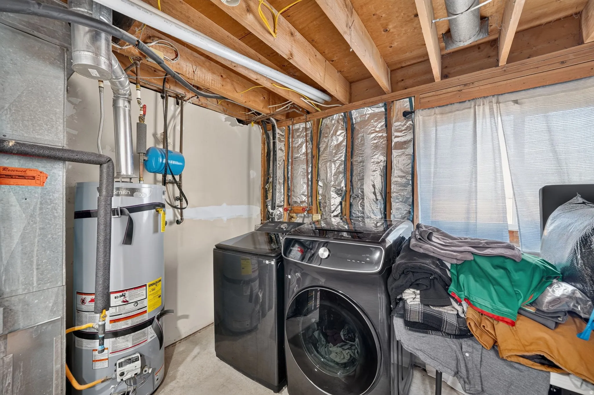Utility area featuring exposed wood ceiling joists, concrete flooring, a water heater, and a washer and dryer