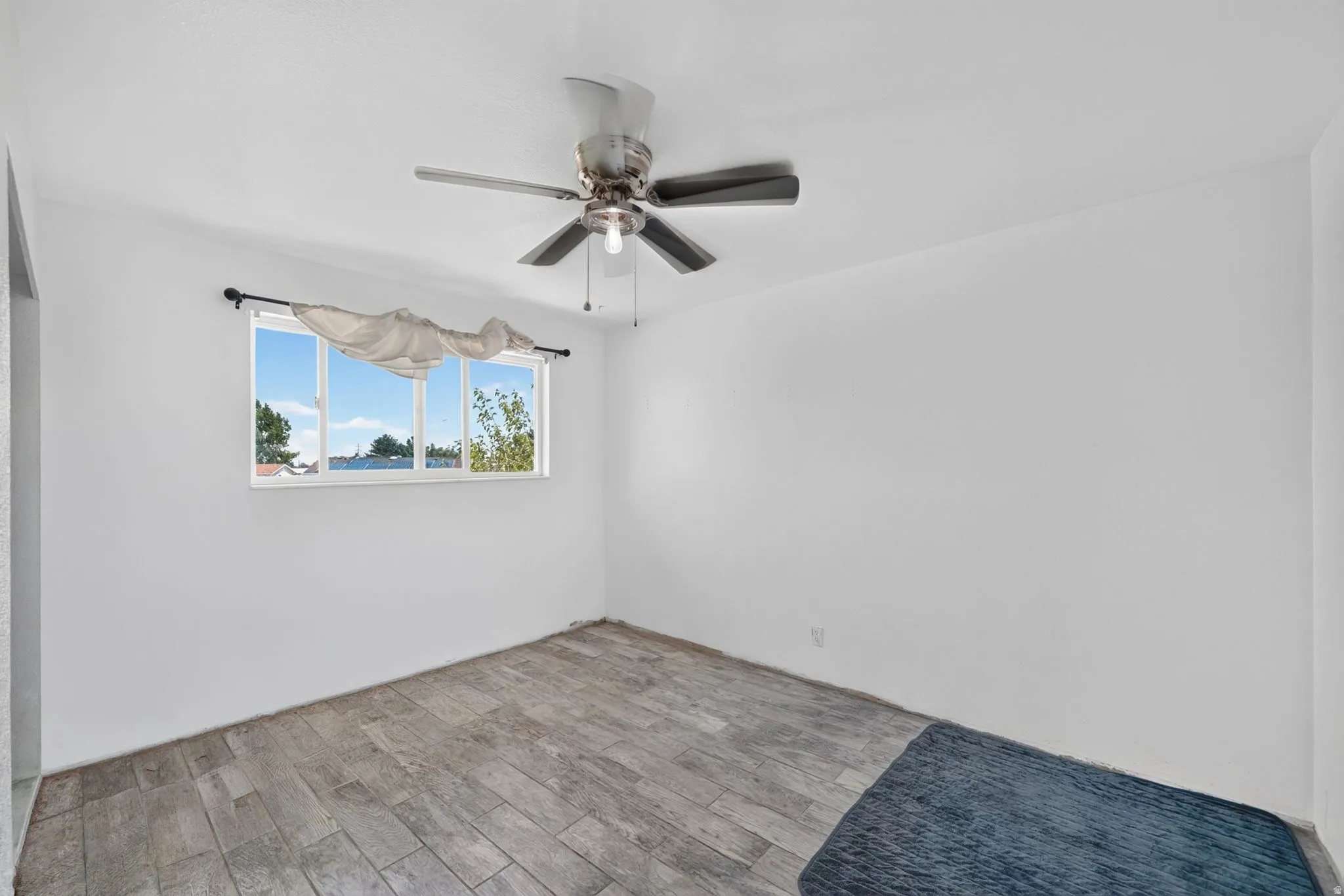 Room featuring wood-finish flooring, a window with outdoor scenery, and a ceiling fan with integrated lighting