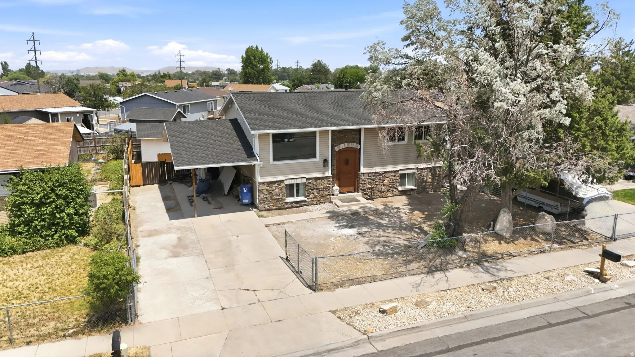 Split-level residence featuring a gray exterior with stone veneer accents, a dark shingle roof, and an attached carport