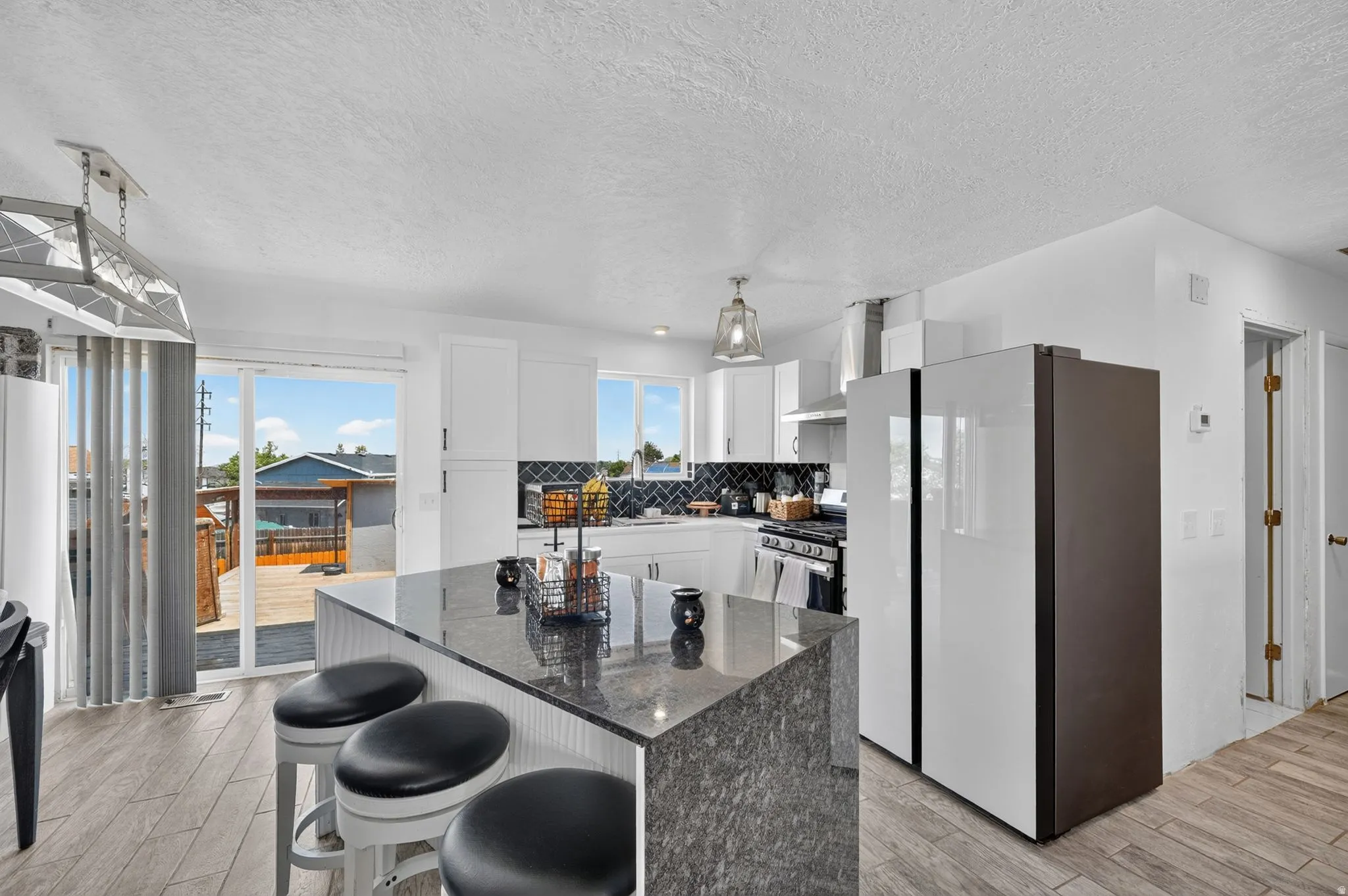 Open-concept kitchen featuring white cabinetry, a dark tile backsplash, stainless steel appliances, and a central island with a granite-style countertop