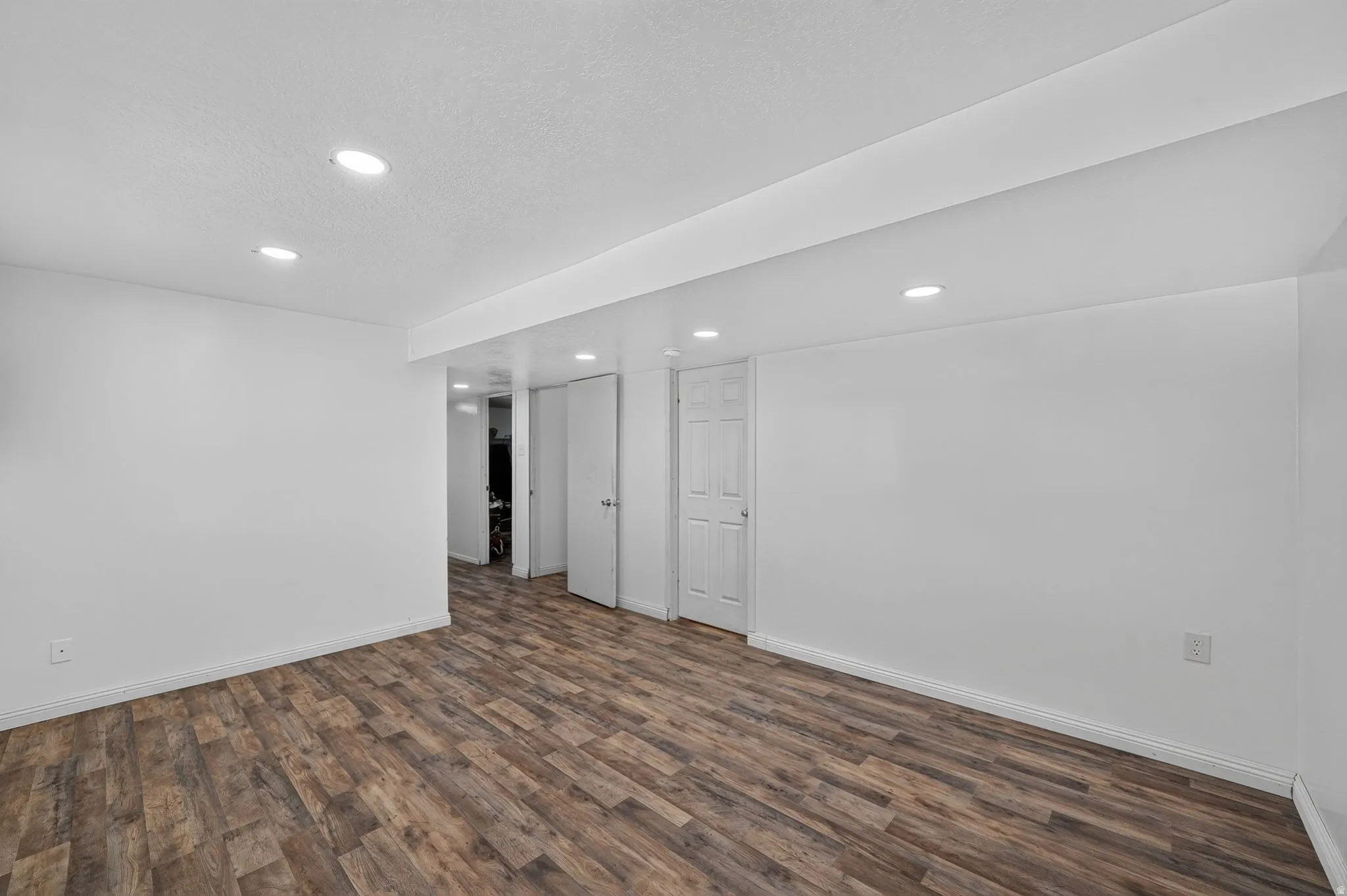 Spacious room featuring wood-finish flooring, white walls, and recessed lighting