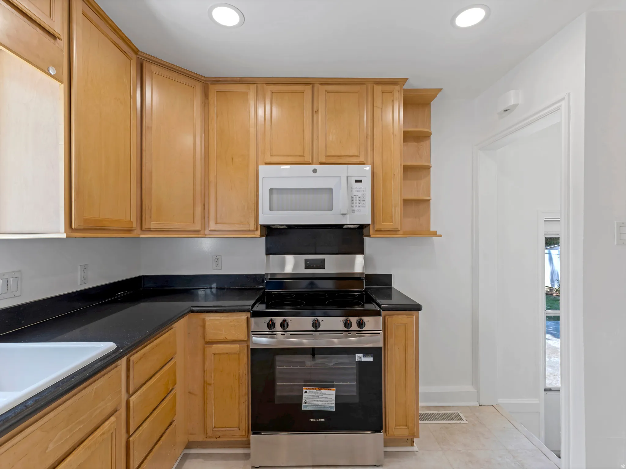 Kitchen featuring wood cabinetry, black countertops, stainless steel range with overhead microwave, and recessed lighting