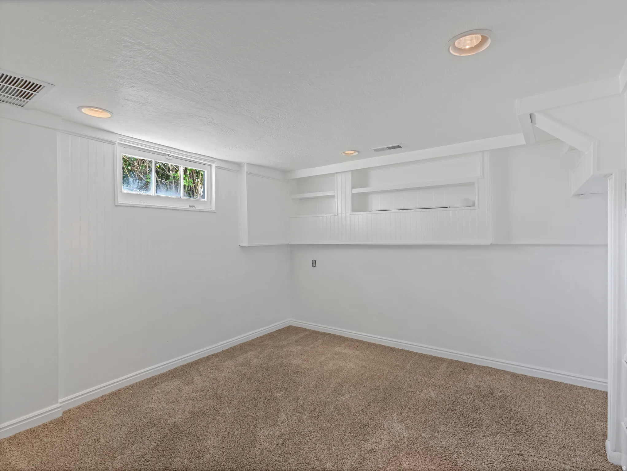 Carpeted room featuring recessed lighting, a window, built-in shelving, white baseboards, and white paneling on a portion of the wall
