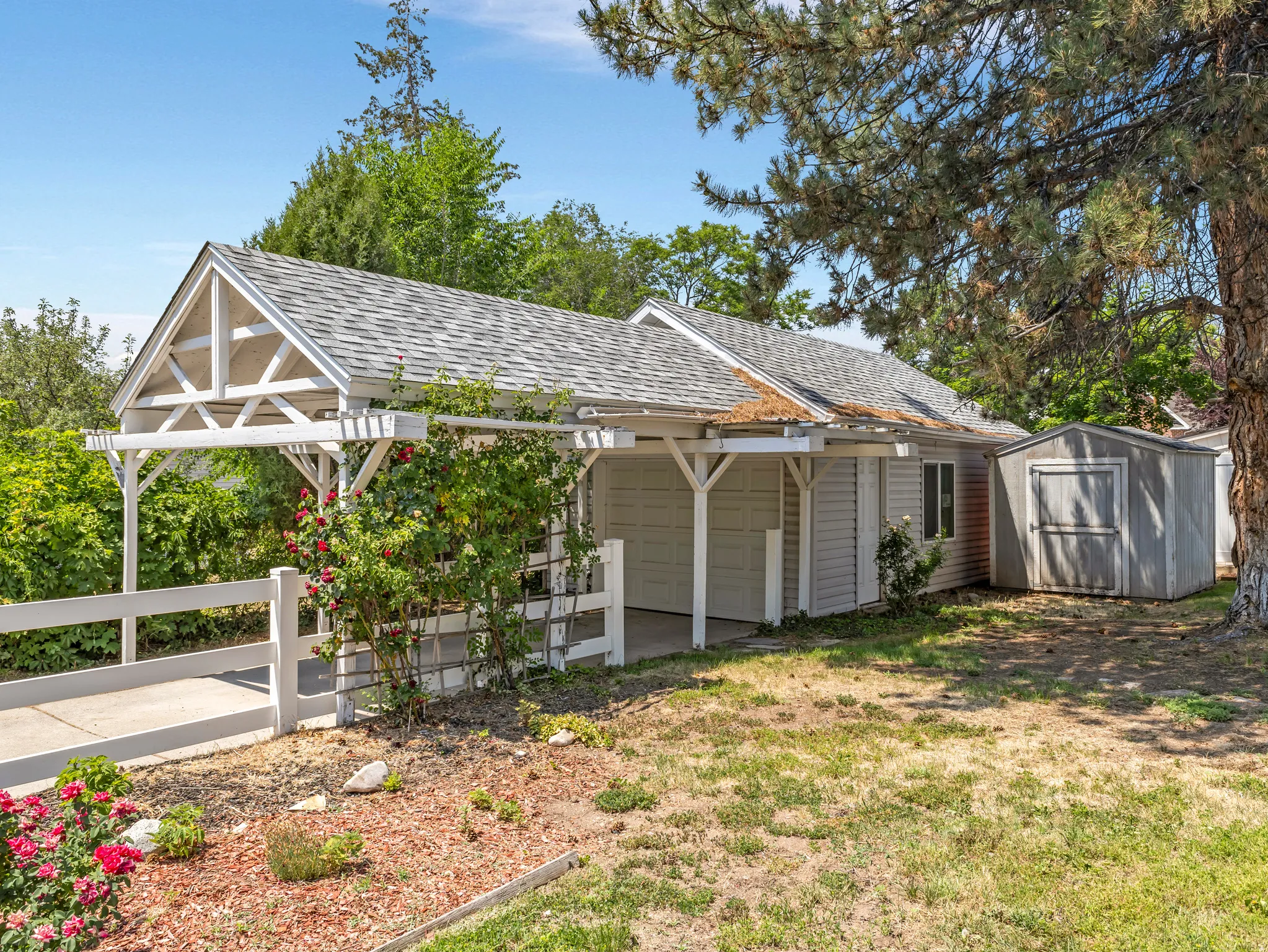 Carport with white pergola structure, asphalt shingle roofing, and white picket fencing