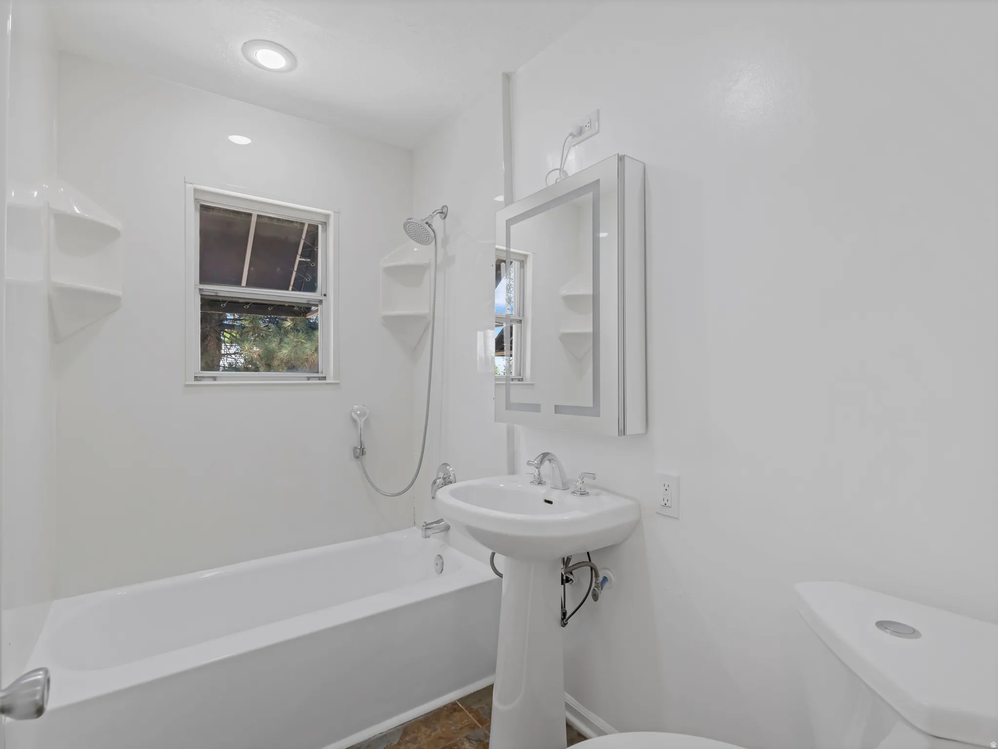 Bathroom featuring a pedestal sink, white toilet, and tub with shower combination
