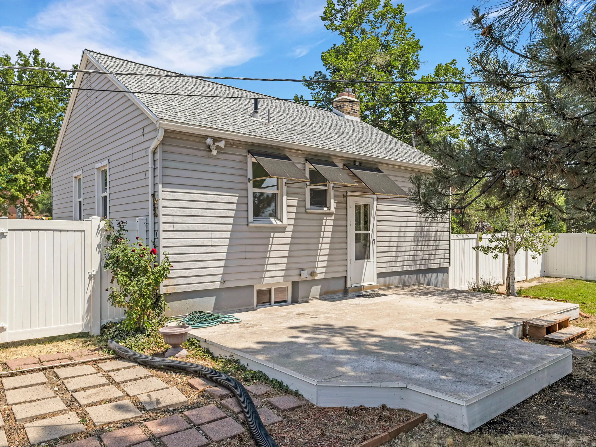 Rear exterior featuring light grey siding, a white screen door, and a concrete patio