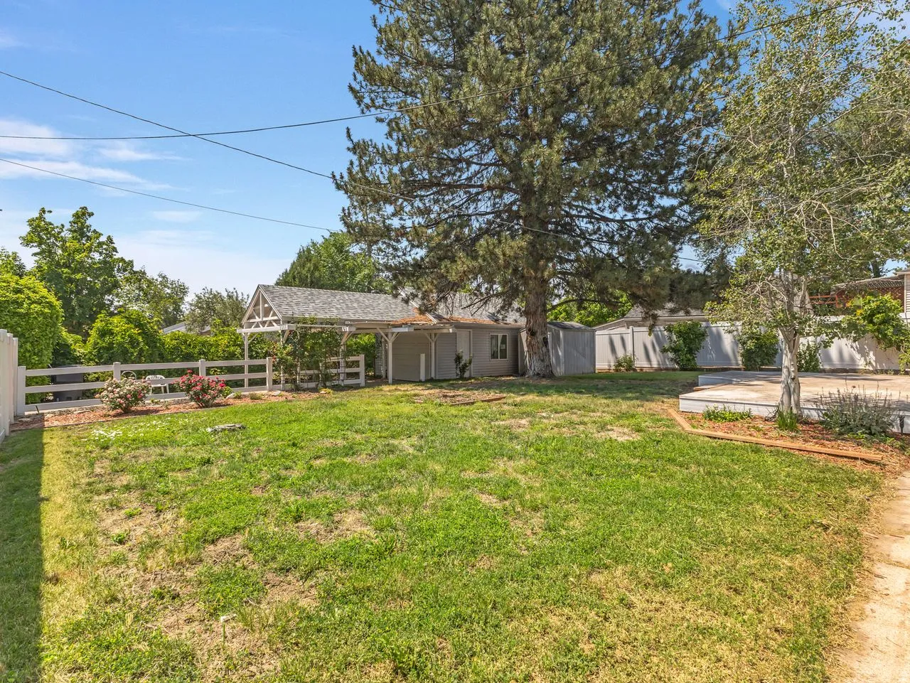 Grassy yard featuring a white picket fence, a covered arbor, and mature trees
