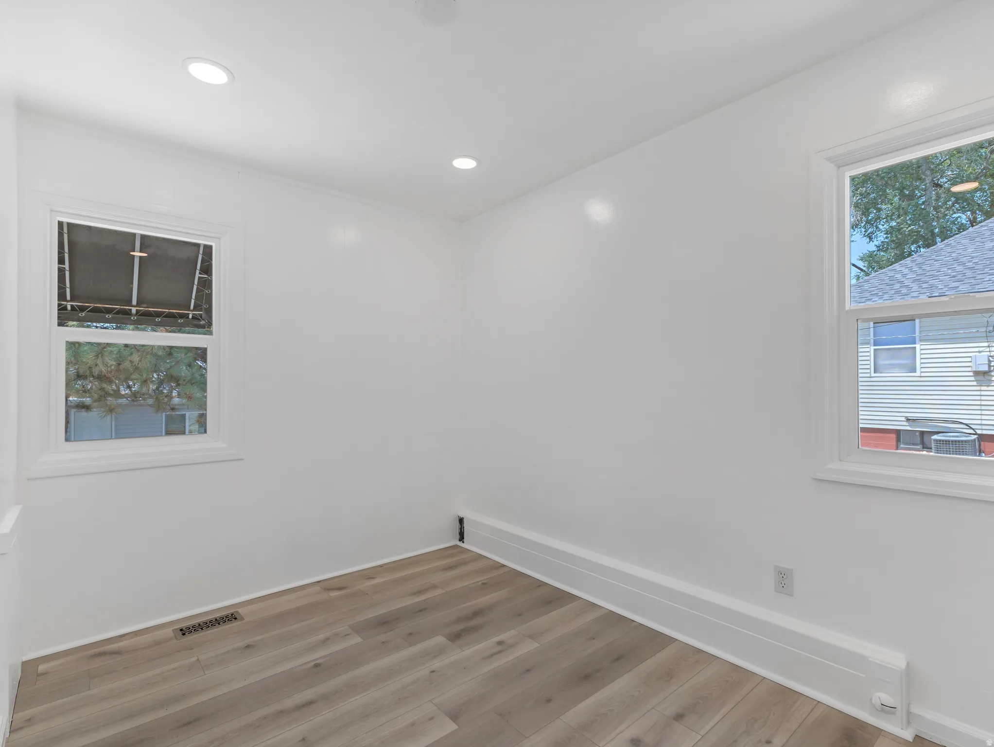 Bright room featuring wood-finish flooring, recessed lighting, white walls, two windows, and baseboard heating