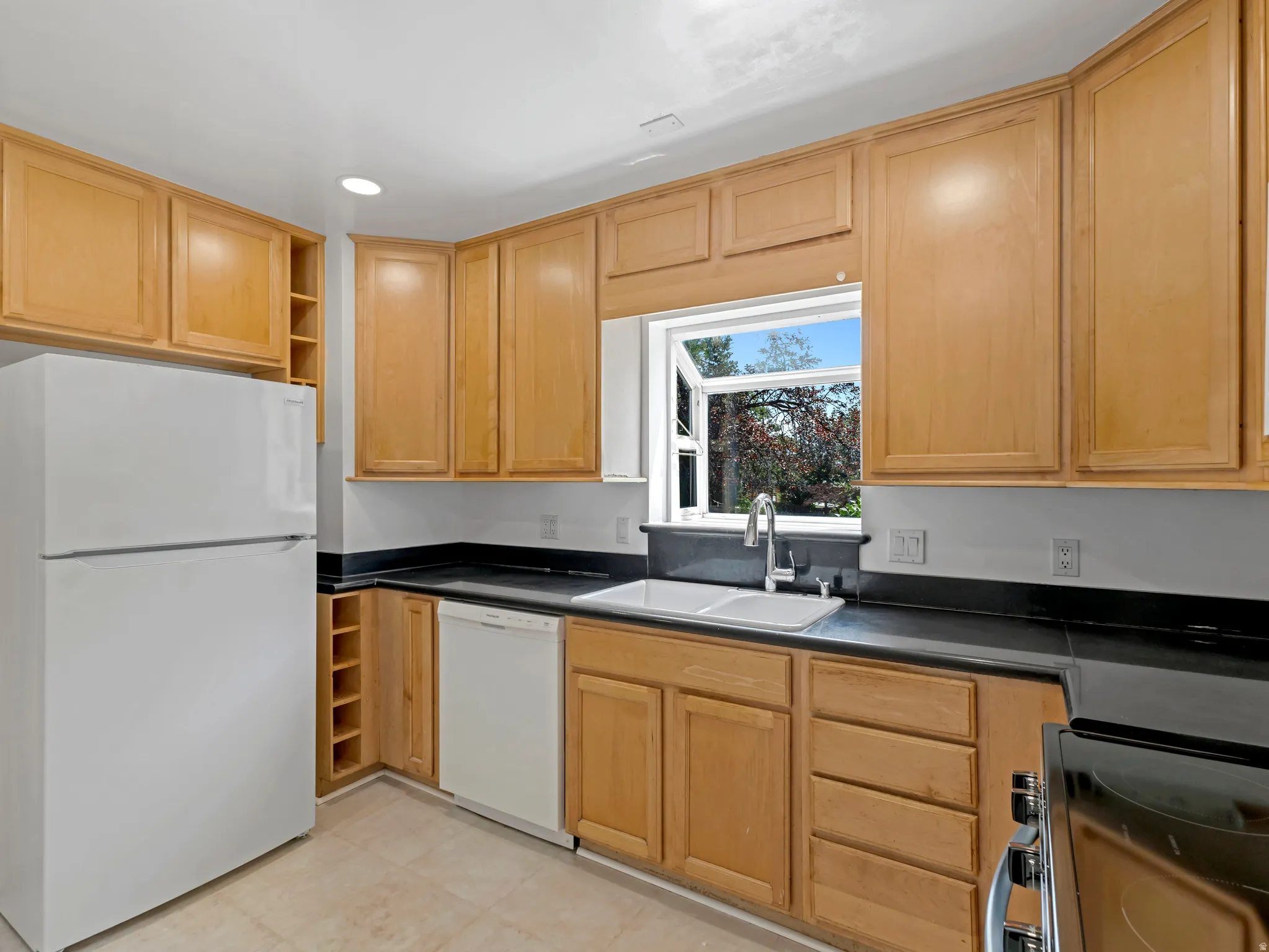 Kitchen featuring wood cabinetry, black countertops, a double basin sink, and a window with exterior greenery