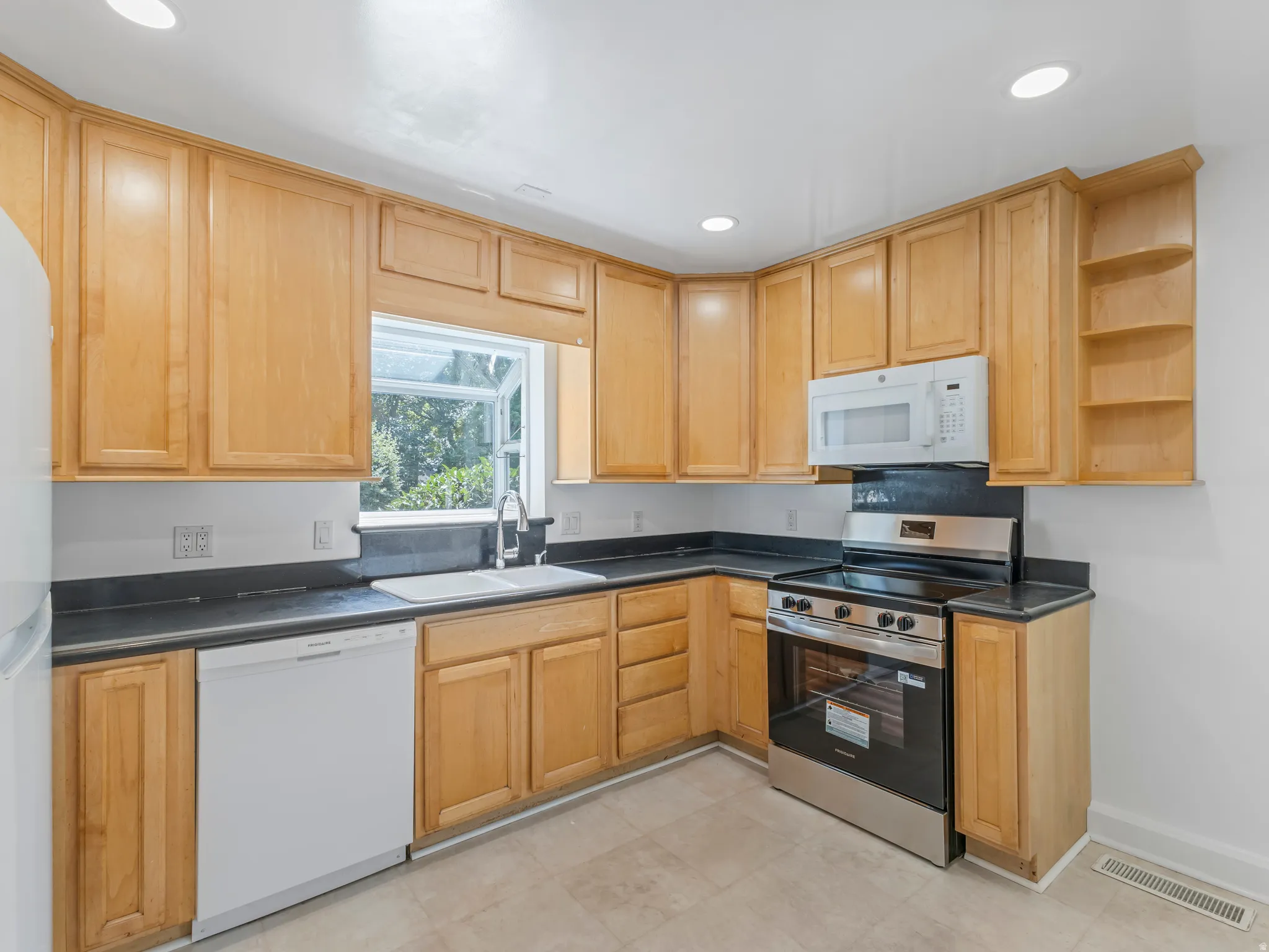 Kitchen featuring light wood cabinetry, dark countertops, a double-basin sink, and stainless steel range with overhead microwave