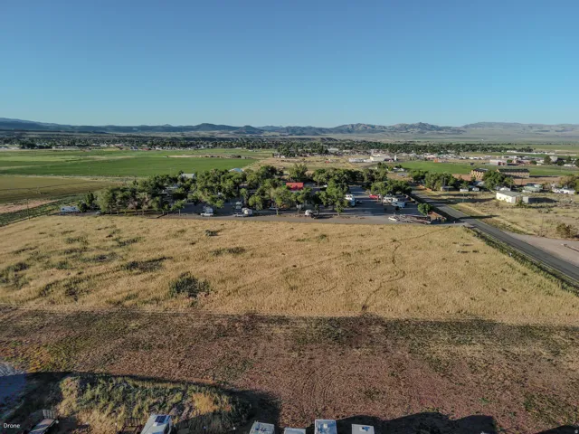 Expansive open land with a distinct foreground of dry grass, bordering a paved road and a cluster of properties featuring mature trees