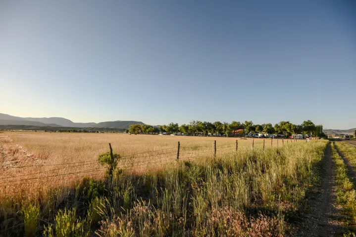 Expansive field with a wire fence, bordered by a dirt path and distant mountains