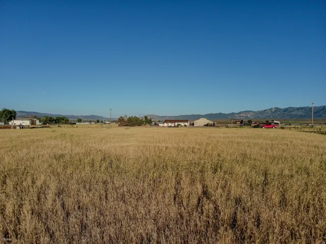 Expansive open field under a clear blue sky, featuring distant structures and mountain ranges