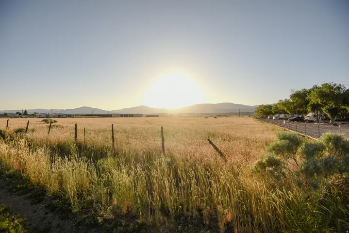 Expansive open field bordered by a rustic wire fence, featuring distant mountains and a clear sky