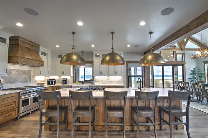 Gourmet kitchen featuring a substantial island with seating, a professional-grade range, a custom wood range hood, pendant lighting, and exposed wooden beams