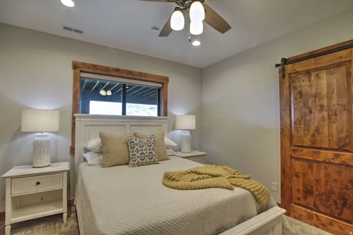 Bedroom featuring a natural wood barn door, a ceiling fan with integrated lighting, and a window with wood-finish trim