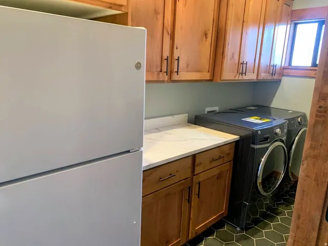 Laundry area featuring wood-finish cabinetry, white countertop, dark hexagonal floor tiles, and a window