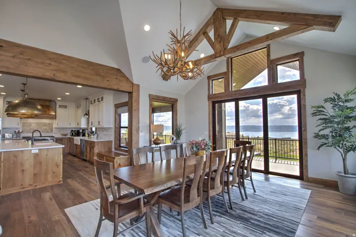 Open-concept living area featuring vaulted ceilings with exposed wood beams, wood-finish flooring, and a contemporary antler chandelier